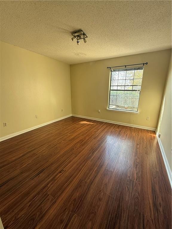 unfurnished room featuring dark wood-style floors, a textured ceiling, and baseboards