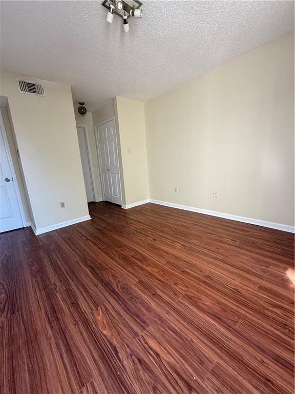 unfurnished room with visible vents, a textured ceiling, dark wood-type flooring, and baseboards