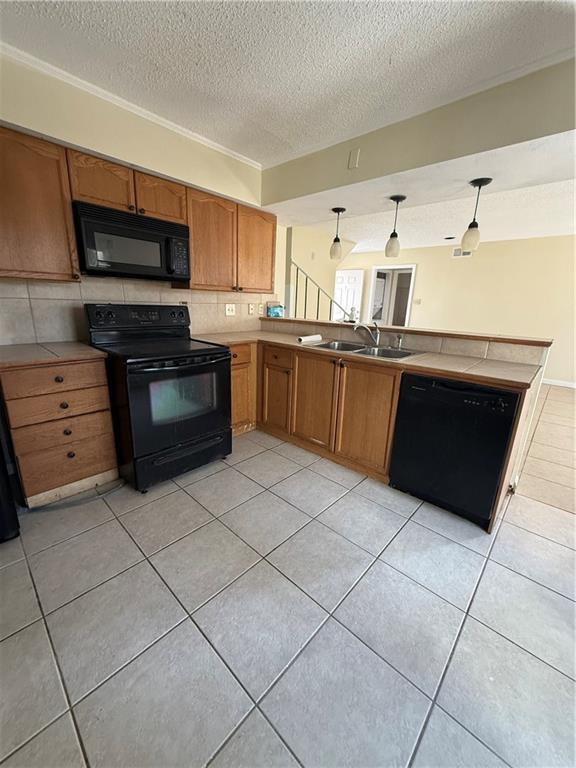 kitchen featuring pendant lighting, a peninsula, brown cabinetry, black appliances, and a sink