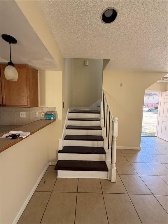 staircase featuring tile patterned floors, a textured ceiling, and baseboards