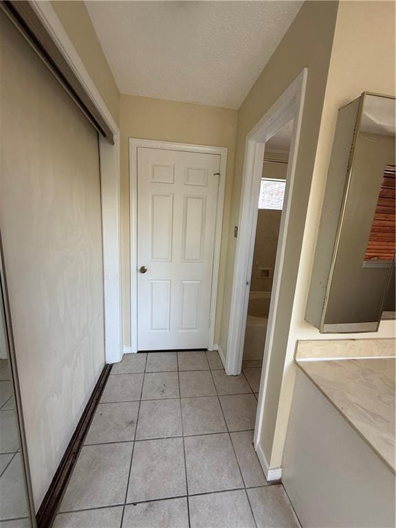 hall with light tile patterned floors, baseboards, and a textured ceiling