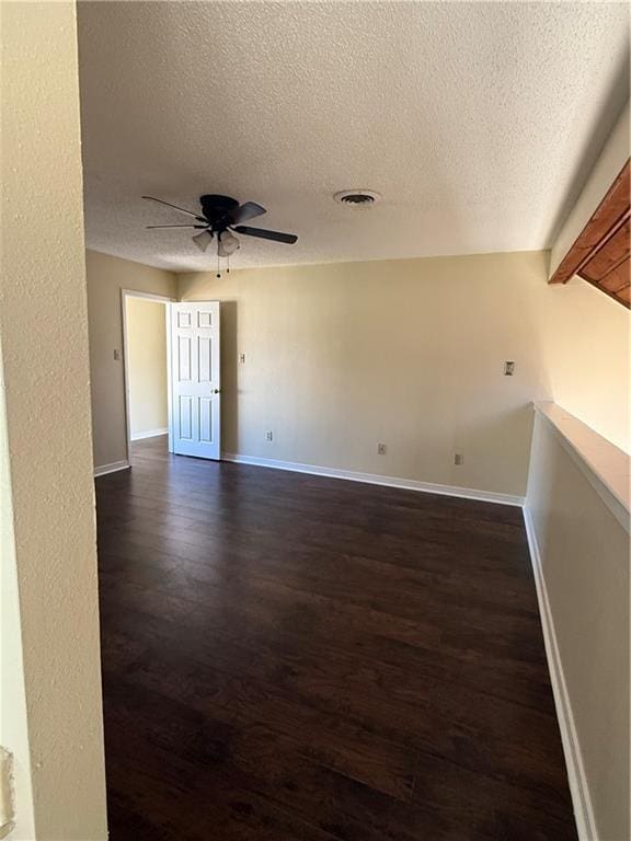 unfurnished room with visible vents, baseboards, ceiling fan, a textured ceiling, and dark wood-style flooring