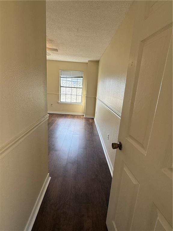 corridor with baseboards, a textured ceiling, a textured wall, and wood finished floors