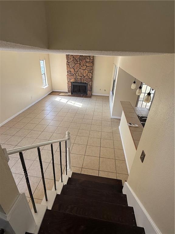 staircase with tile patterned flooring, a stone fireplace, a high ceiling, and baseboards