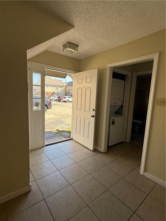 foyer with light tile patterned flooring, a textured ceiling, stacked washing maching and dryer, and baseboards