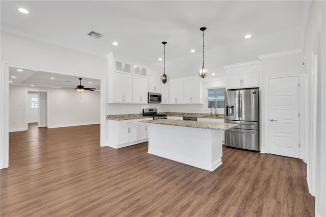 kitchen with a sink, a kitchen island, wood finished floors, stainless steel appliances, and white cabinets