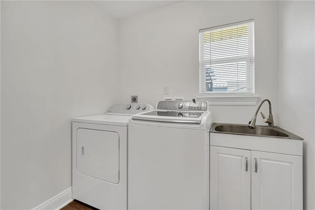 clothes washing area with a sink, baseboards, cabinet space, and separate washer and dryer