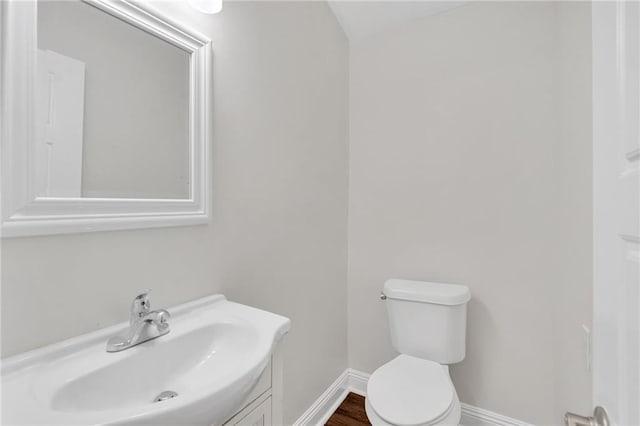 half bathroom with vanity, toilet, and baseboards