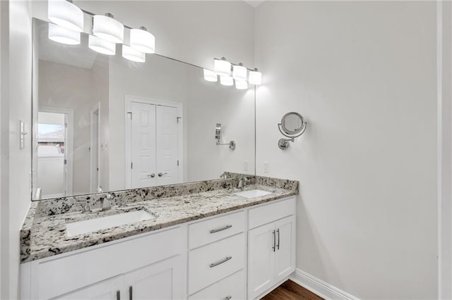 full bath with double vanity, wood finished floors, baseboards, and a sink