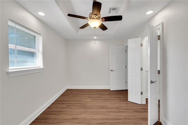 unfurnished bedroom with visible vents, baseboards, a tray ceiling, recessed lighting, and wood finished floors