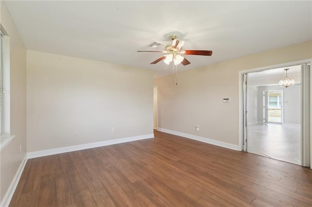 spare room with baseboards, wood finished floors, and ceiling fan with notable chandelier