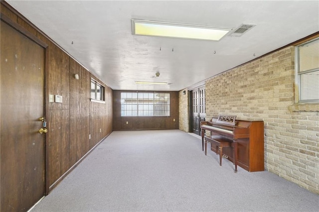 living area featuring visible vents, carpet, brick wall, and wood walls