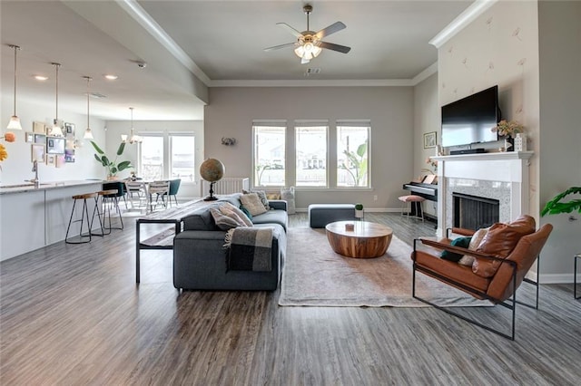 living room featuring a high end fireplace, baseboards, ornamental molding, ceiling fan with notable chandelier, and wood finished floors