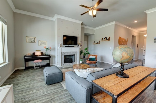 living area with baseboards, ornamental molding, a fireplace, wood finished floors, and a ceiling fan