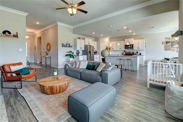 living room with baseboards, visible vents, light wood-style flooring, recessed lighting, and crown molding