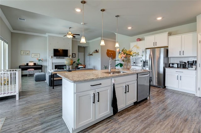 kitchen with visible vents, a fireplace, a kitchen island with sink, a sink, and appliances with stainless steel finishes