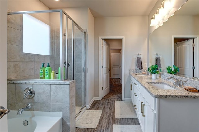 full bath featuring a garden tub, double vanity, a stall shower, wood finished floors, and a sink