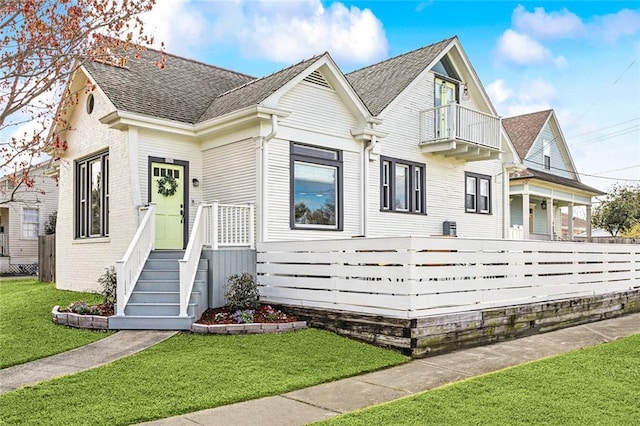 view of front of home featuring a front lawn, a balcony, brick siding, and a shingled roof