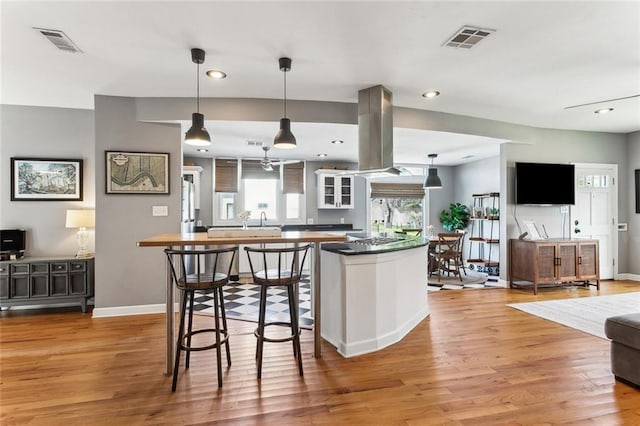 kitchen with dark countertops, visible vents, island exhaust hood, and light wood-style floors