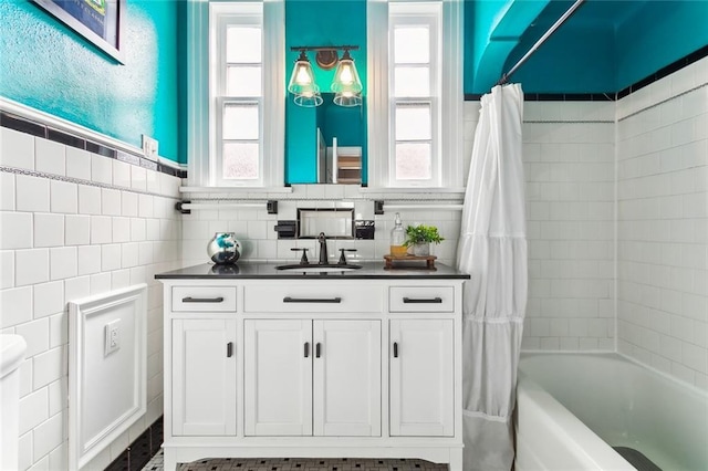 full bath featuring a wealth of natural light, vanity, shower / bath combo with shower curtain, and tile walls