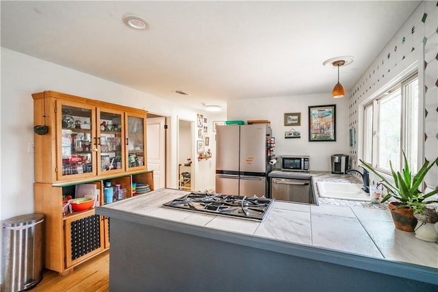 kitchen featuring a peninsula, a sink, stainless steel appliances, tile counters, and glass insert cabinets