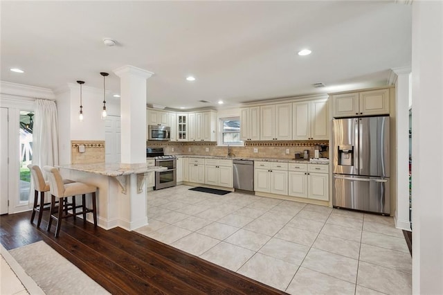 kitchen with light stone counters, a peninsula, a sink, stainless steel appliances, and tasteful backsplash