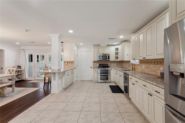 kitchen featuring light stone counters, decorative backsplash, a peninsula, stainless steel appliances, and a sink