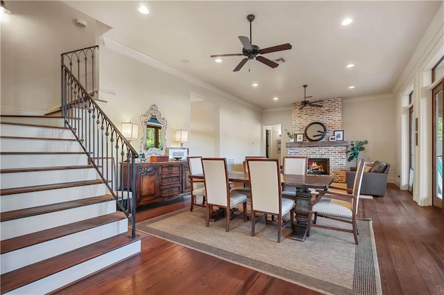 dining room featuring hardwood / wood-style floors, recessed lighting, ornamental molding, stairs, and a brick fireplace