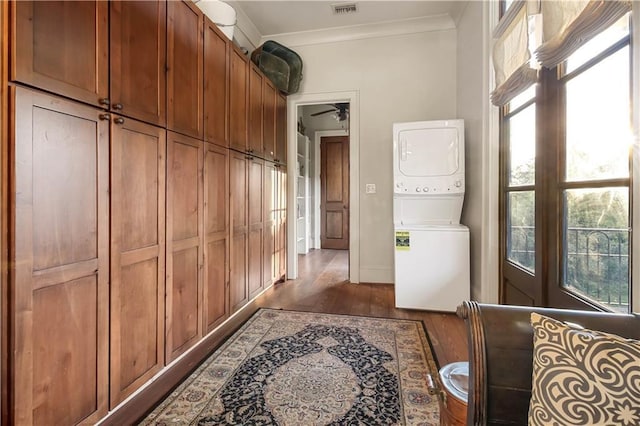 laundry room with crown molding, dark wood-type flooring, laundry area, stacked washer and clothes dryer, and plenty of natural light