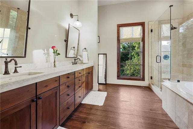 full bathroom featuring a garden tub, double vanity, a stall shower, wood finished floors, and a sink