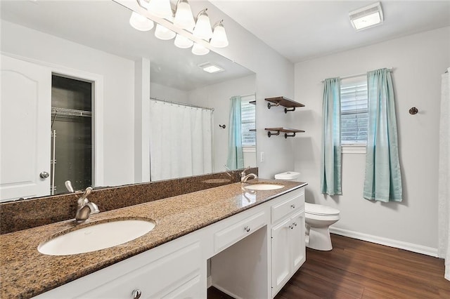 full bath featuring baseboards, toilet, double vanity, wood finished floors, and a sink