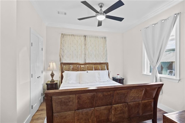 bedroom with visible vents, ornamental molding, wood finished floors, baseboards, and ceiling fan