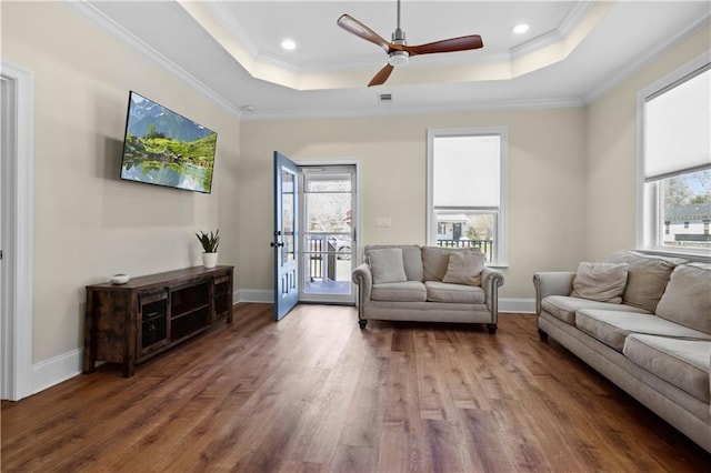 living room with a wealth of natural light, crown molding, a raised ceiling, and wood finished floors