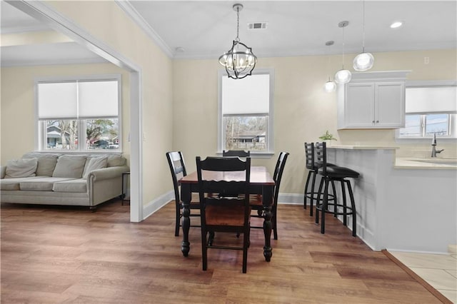 dining room featuring visible vents, plenty of natural light, ornamental molding, and light wood-style flooring