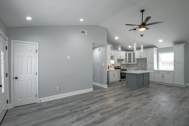 kitchen featuring visible vents, under cabinet range hood, gas range, vaulted ceiling, and white cabinetry