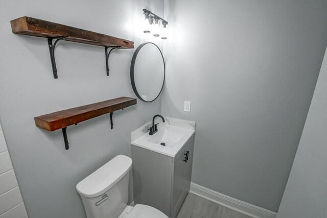 half bathroom with baseboards, toilet, wood finished floors, and vanity