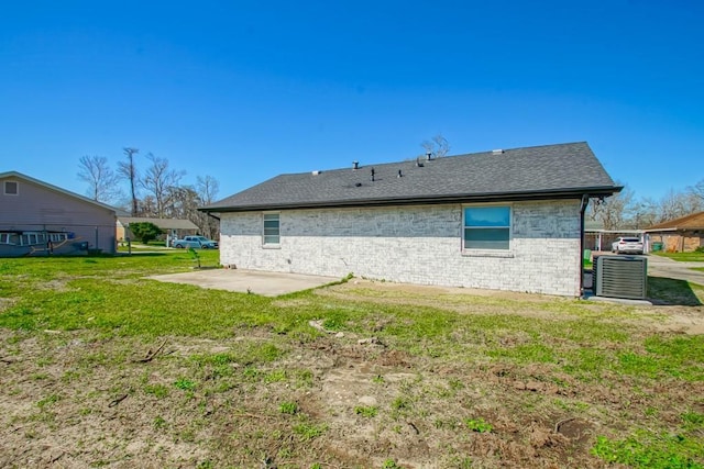 back of property with brick siding, roof with shingles, cooling unit, a yard, and a patio area