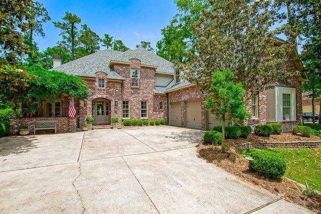 view of front of home with driveway, a shingled roof, a garage, brick siding, and a chimney