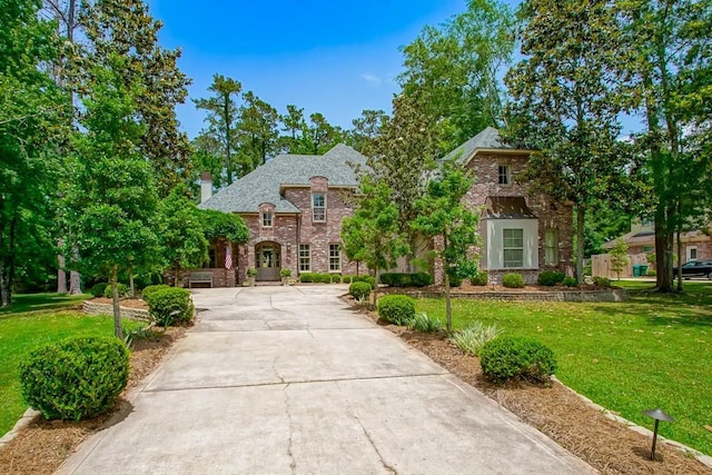 view of front of home with driveway, brick siding, a chimney, and a front lawn