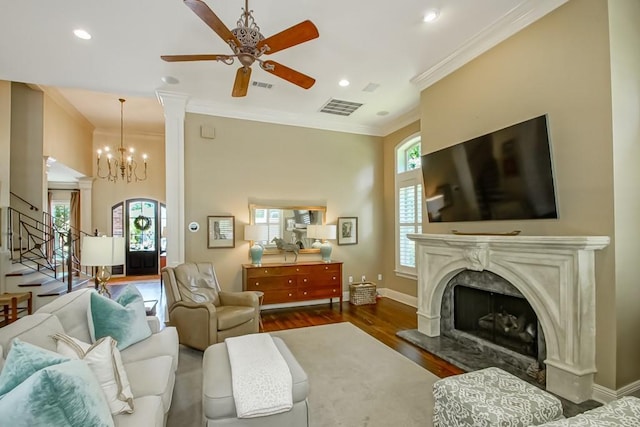 living room featuring visible vents, ornamental molding, ceiling fan with notable chandelier, wood finished floors, and stairway