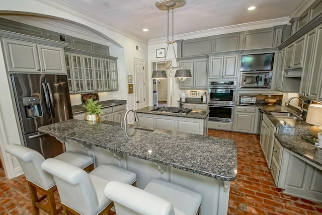 kitchen featuring a sink, appliances with stainless steel finishes, a kitchen island with sink, and ornamental molding