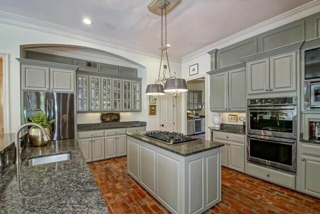 kitchen with a kitchen island, glass insert cabinets, crown molding, stainless steel appliances, and a sink