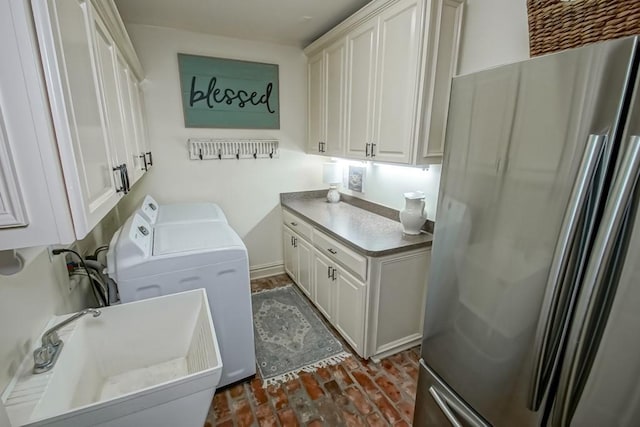 clothes washing area with independent washer and dryer, cabinet space, brick floor, and a sink