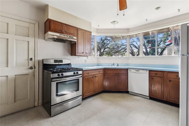 kitchen featuring under cabinet range hood, light countertops, brown cabinets, white appliances, and a sink