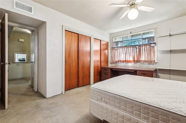 bedroom featuring a ceiling fan, light colored carpet, visible vents, and two closets