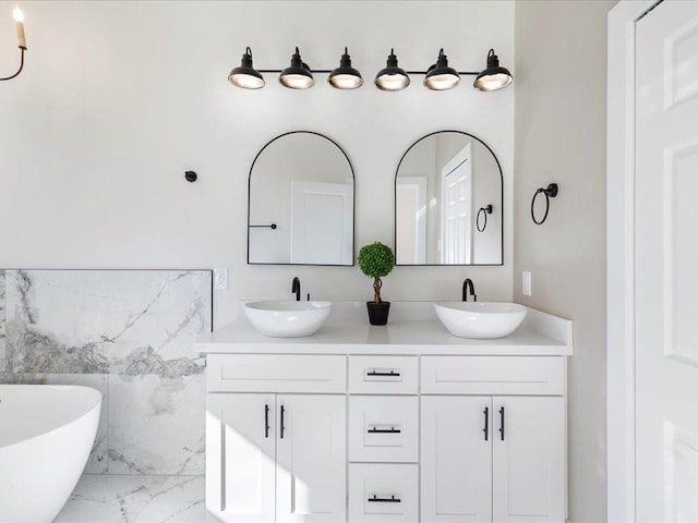 bathroom featuring a sink, a soaking tub, marble finish floor, and double vanity