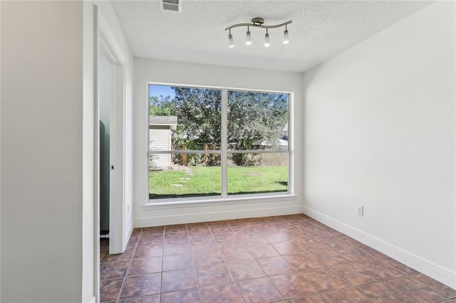 empty room with tile patterned floors, visible vents, a textured ceiling, and baseboards