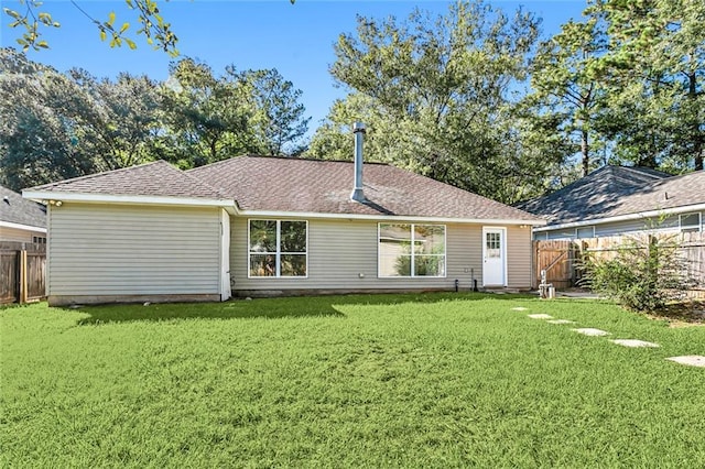 rear view of house with a lawn, a shingled roof, and a fenced backyard