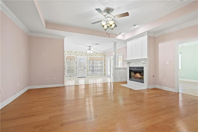 unfurnished living room featuring a fireplace with flush hearth, crown molding, light wood-style floors, and decorative columns