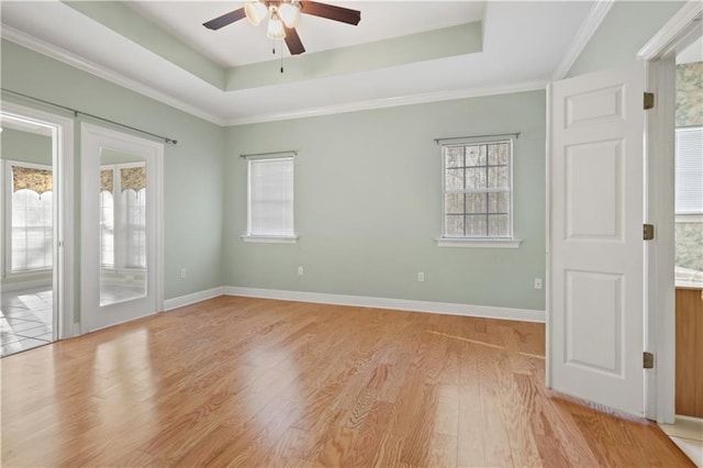 spare room featuring light wood finished floors, ceiling fan, a raised ceiling, and baseboards